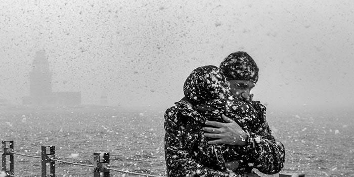 Sich umarmendes Paar im Schneegestöber am Meer